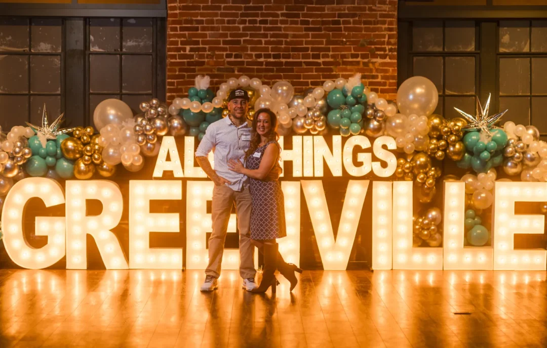 events-7 A couple poses in front of illuminated “ALL THINGS GREENVILLE” sign with balloon decorations.