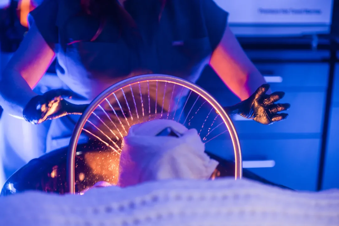 health-wellness-14 Person in gloves performs therapy on a person with a towel on their head, illuminated by blue and orange light.