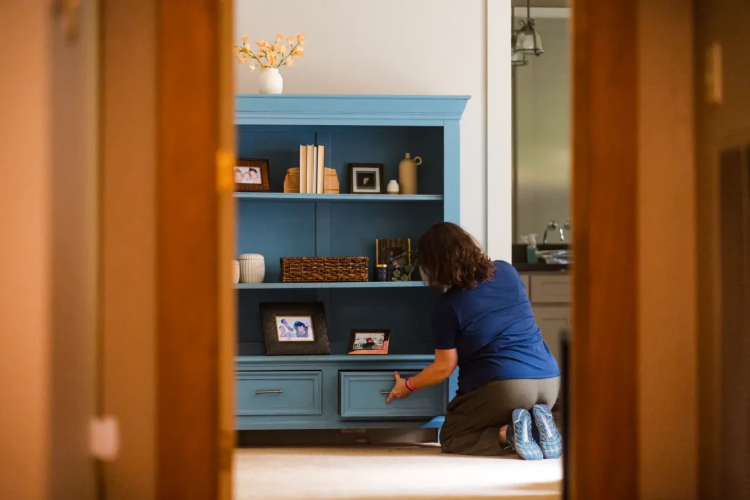 professional-7 Person kneeling in front of a blue shelf, arranging items and photos in a warmly lit room.