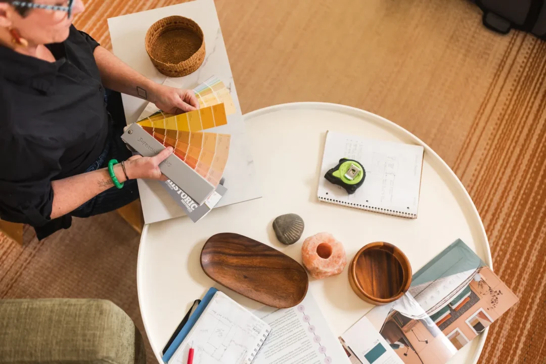 professional-9 Person holding paint swatches over a table with notebooks, a tape measure, bowls, and design materials.