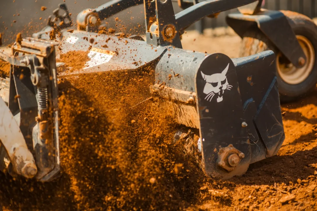 trades-25 Close-up of a machine tilling soil, with dirt flying, and a Bobcat logo visible on the equipment.