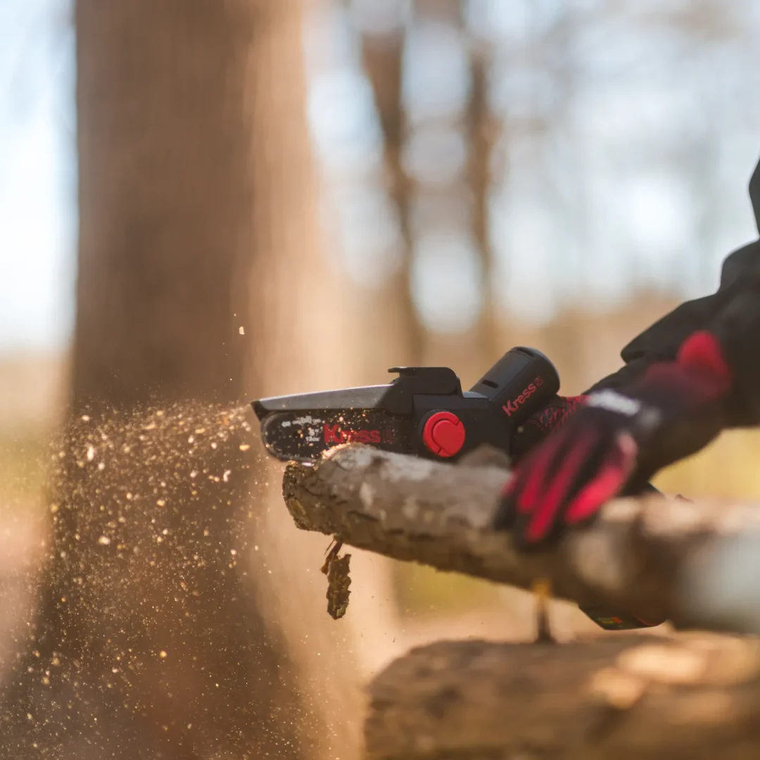 trades-32 A gloved hand uses a chainsaw to cut a tree branch, with sawdust flying in the sunlight.