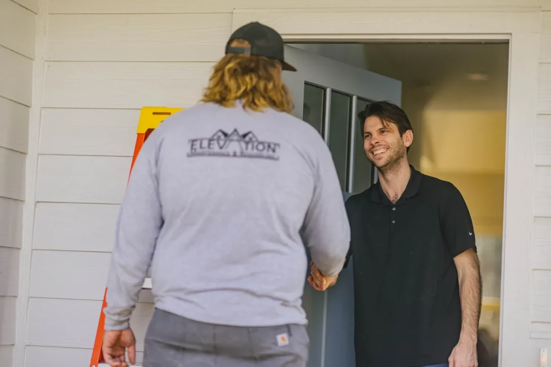 trades-35 A man in a black shirt smiles and greets another man wearing an “Elevation” sweatshirt at the door.