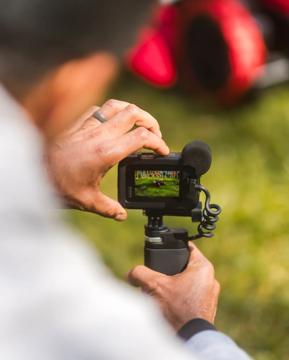 video-1 Person filming red object outdoors with a handheld camera on a grassy field, image focused on the camera screen.