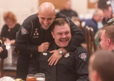 Two uniformed officers laugh together at a table during a formal dining event.