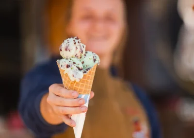 A person in an apron holds out an ice cream cone with three scoops toward the camera.
