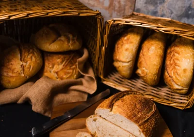 Sliced and whole loaves of bread on a wooden board, with baskets of bread in the background.