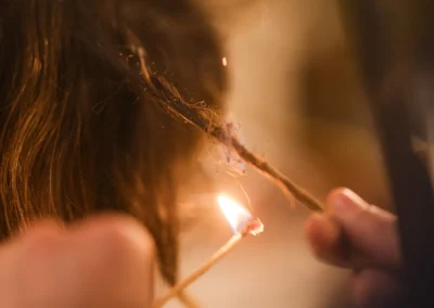 A person burning the tip of a hair strand with a small flame, performing a hair treatment.
