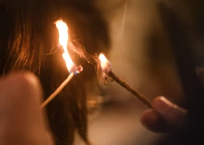 Close-up of a person burning hair with two lit sticks, possibly during a hair treatment or ritual.