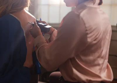 Person marking another’s back with a pen while holding a device, sunlight shining through window behind.
