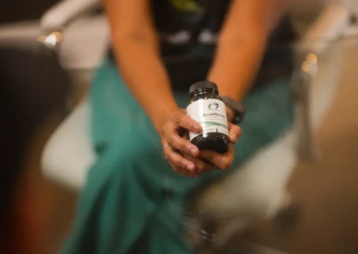 A person holds a bottle of supplements labeled “AlluGenix” while sitting at a glass table.