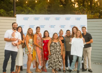 A group of people smiling and posing together in front of an American Cancer Society backdrop outdoors.