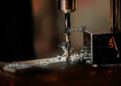 A close-up of a drill bit creating metal shavings while drilling into a metal surface.