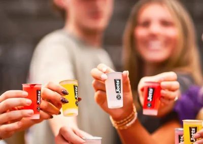 People holding up colorful Jello shots, smiling and celebrating together.