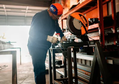 A person wearing gloves uses a miter saw to cut metal in a workshop.