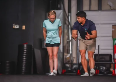 A woman and man practice balance exercises together indoors on a gym mat, both focused and barefoot.