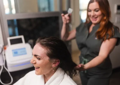 Smiling woman in a white robe gets her hair washed by a stylist in a salon.