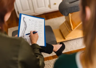 A person holds a spine diagram and notes, sitting near another person in a medical office.
