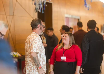 People talking and smiling in a modern indoor space, with a woman in red and a man in patterned shirt.