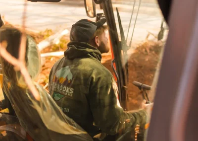Man wearing a cap and hoodie operates machinery, viewed through a window with reflections and sunlight.
