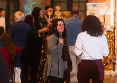 People standing and talking at an indoor event with warm lighting and festive gold decorations.