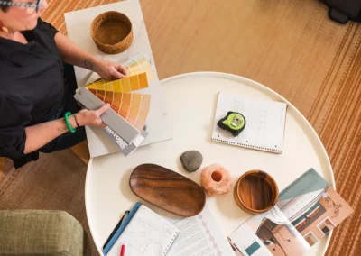 Person selecting paint swatches at a table with notebooks, decor items, and design plans.