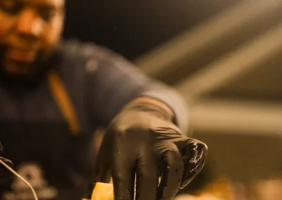 A chef wearing black gloves places food onto a stacked white plate under warm lighting.