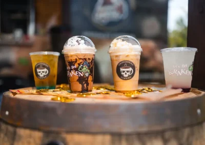 Four specialty drinks with pirate-themed logos on a wooden barrel, surrounded by gold coins.