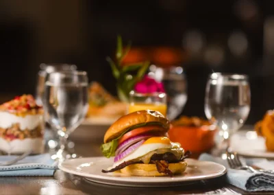 A cheeseburger with lettuce, tomato, and onion on a plate, surrounded by water glasses and desserts.
