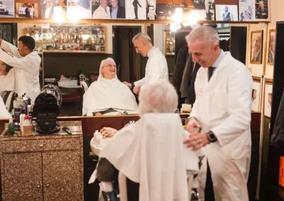 Barbershop with barbers in white coats cutting hair; walls covered with framed photos and mirrors.