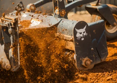 Close-up of machinery digging and kicking up orange dirt, with the Bobcat logo visible on the side.