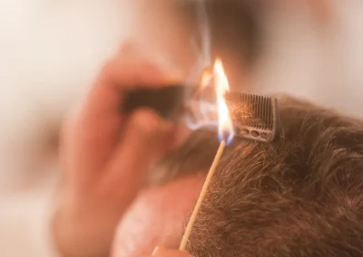 Close-up of a person burning hair on a comb with a lit stick during a hair treatment.