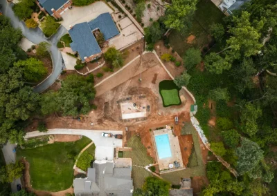 Aerial view of a suburban area with houses, a pool, trees, and a construction site.