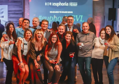 A group of people posing and smiling together at an indoor event with drinks in their hands.