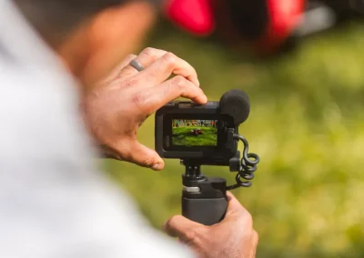 Person filming outdoors with a handheld camera, focusing on a red object on the grass.