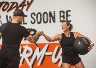 Two people fist bump. One holds a medicine ball. Bold “warm-up” text is painted on the wall behind them.