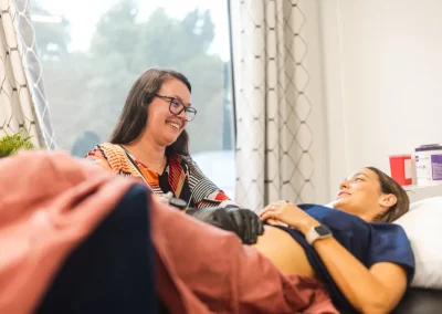 A doctor performs an ultrasound on a smiling pregnant woman lying on an exam table in a clinic.