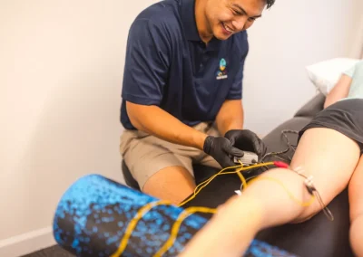 Smiling therapist applies electrodes to a person’s leg during a physical therapy session.