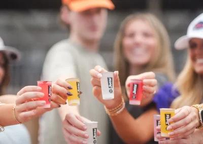 Four people holding up colorful SPF 30 sunscreen shots, smiling and celebrating outdoors.