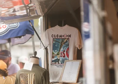 A Clemson t-shirt displayed at an outdoor market booth, with other merchandise and signs visible around it.