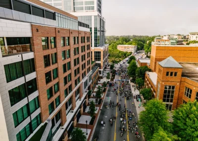 Aerial view of a city street with people marching between tall buildings and green trees.