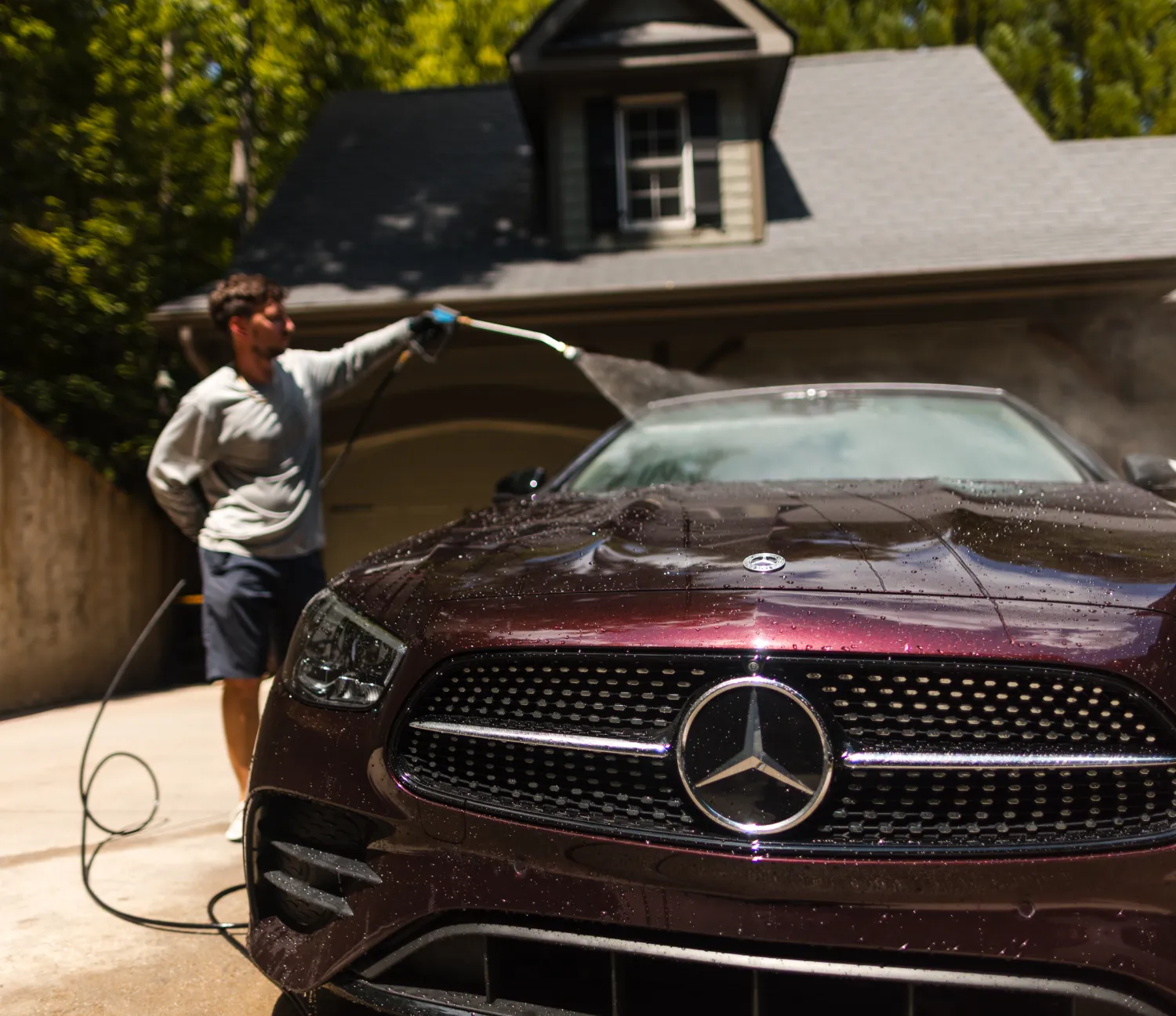 auto-1-1 A person pressure washing a dark maroon Mercedes-Benz in a driveway.