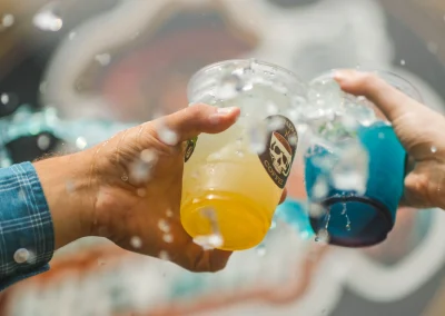 Two hands holding plastic cups containing yellow and blue drinks during a splash.