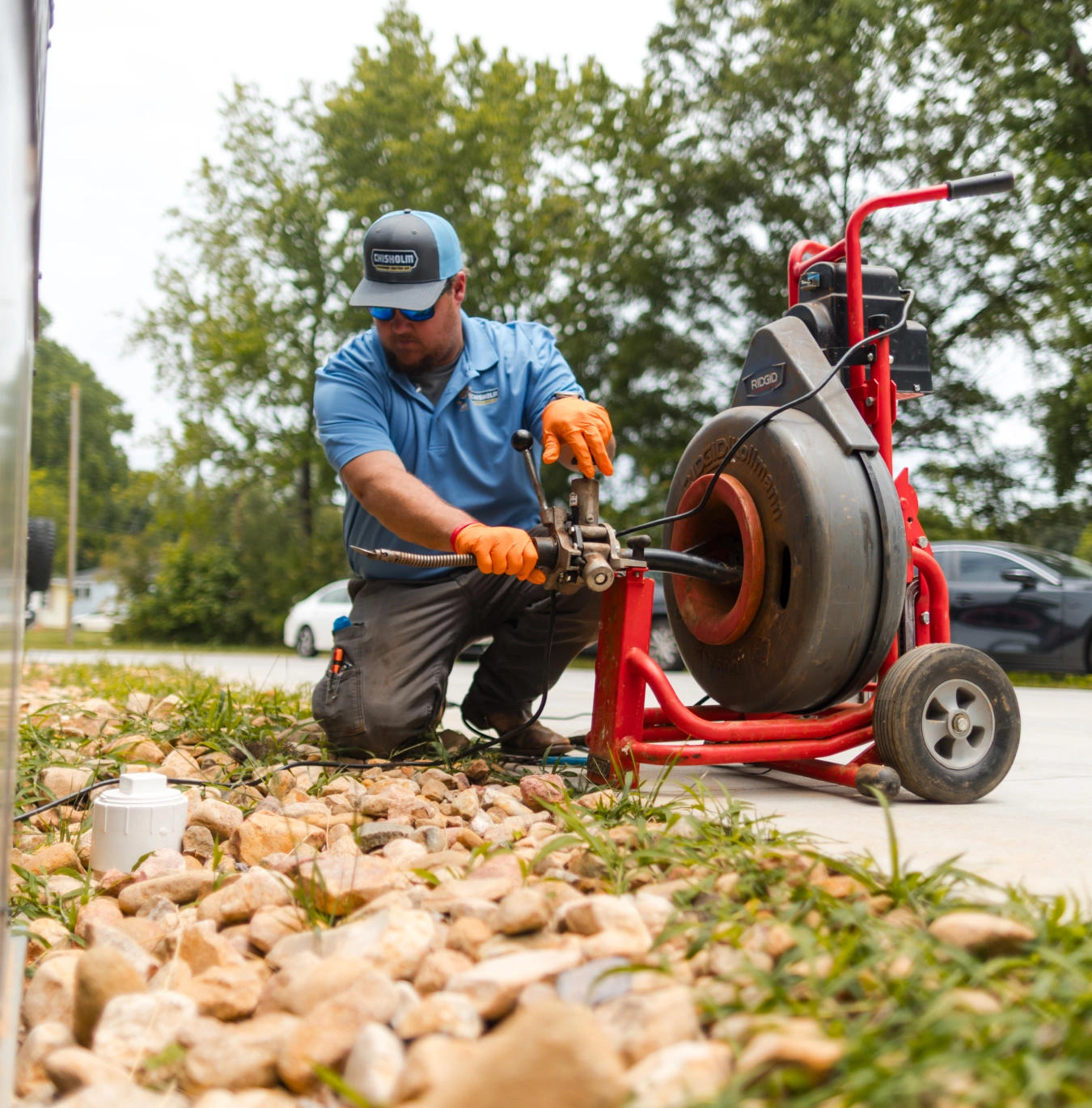 chisholm-plumbing-2 A technician in a blue shirt uses a professional drain cleaning machine outdoors.