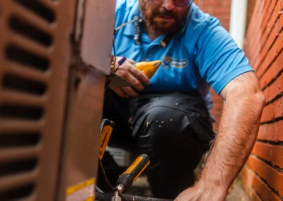 Technician in a blue shirt repairing an outdoor air conditioning unit.