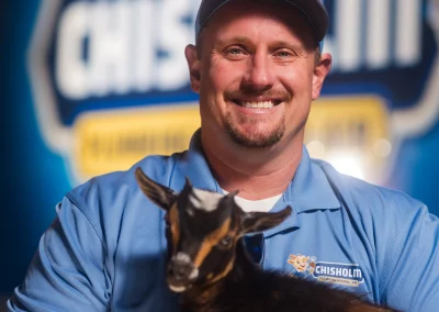 A man in a Chisholm Plumbing uniform holding a baby goat.