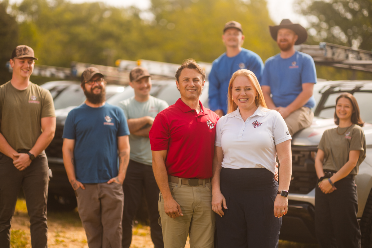 precision-pest-2 A group of eight people wearing branded work uniforms posing in front of pickup trucks.
